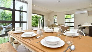 A dining area with a long wooden table set for a meal, large windows, and a view of greenery outside. - Hagley Apartment (Christchurch)