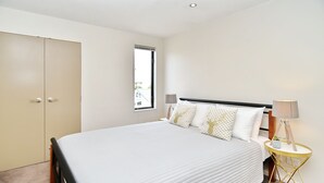 A bedroom with a bed, bedside tables, a wardrobe, and a window. - Hagley Apartment (Christchurch)