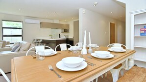 A dining area with a wooden table set for four, white chairs, and a kitchen in the background. - Hagley Apartment (Christchurch)