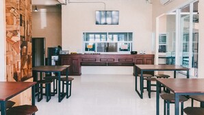 A modern cafe with wooden walls, a central counter, and multiple tables and chairs. - More than Sleep Hostel Pak Chong - Khao Yai (Pak Chong)