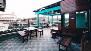 A rooftop terrace with wooden tables and benches, a checkered floor, and a view of buildings in the background. - More than Sleep Hostel Pak Chong - Khao Yai (Pak Chong)