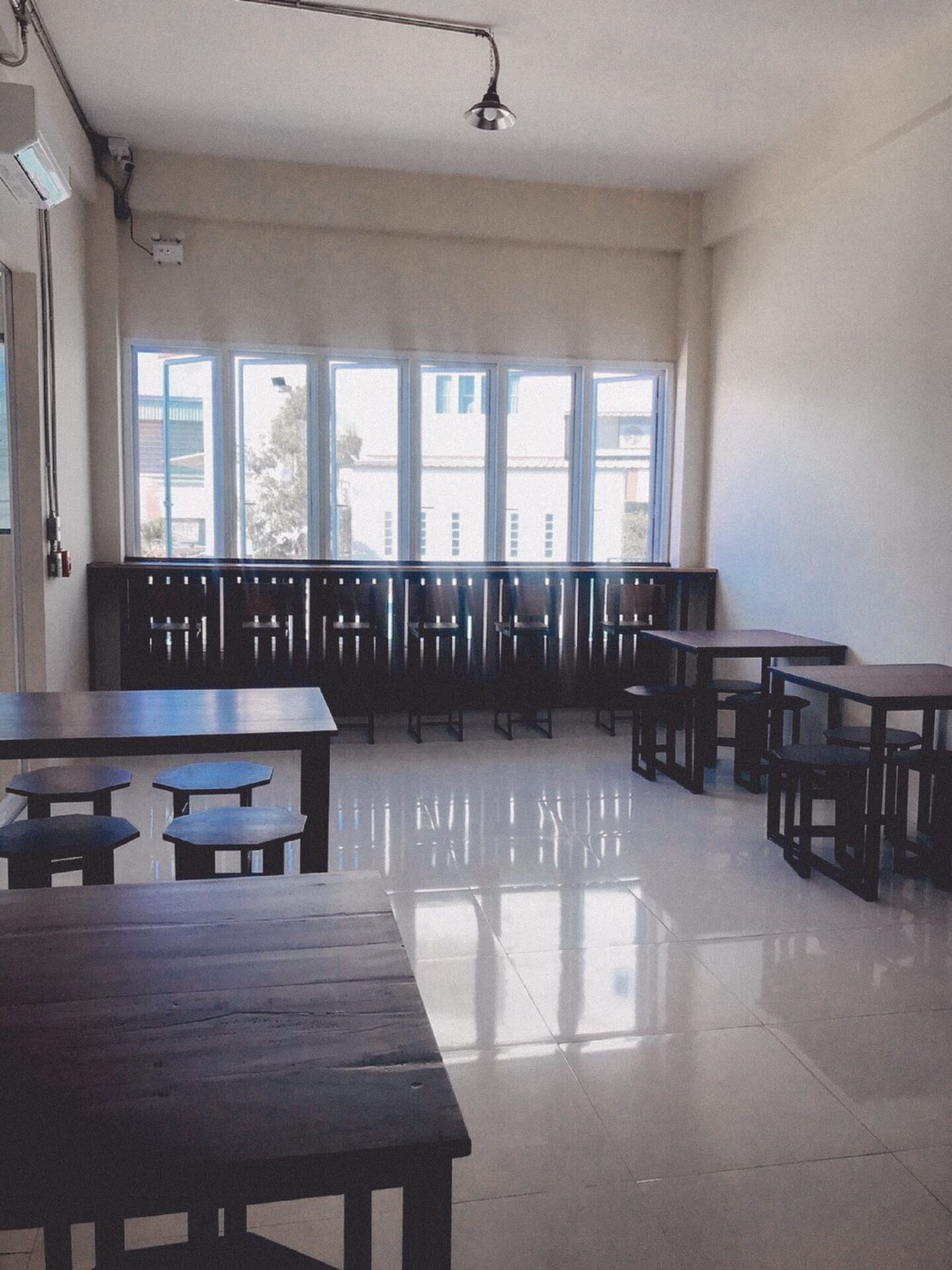 Un aula con varias mesas y bancos, ventanas amplias y un piso limpio de baldosas.