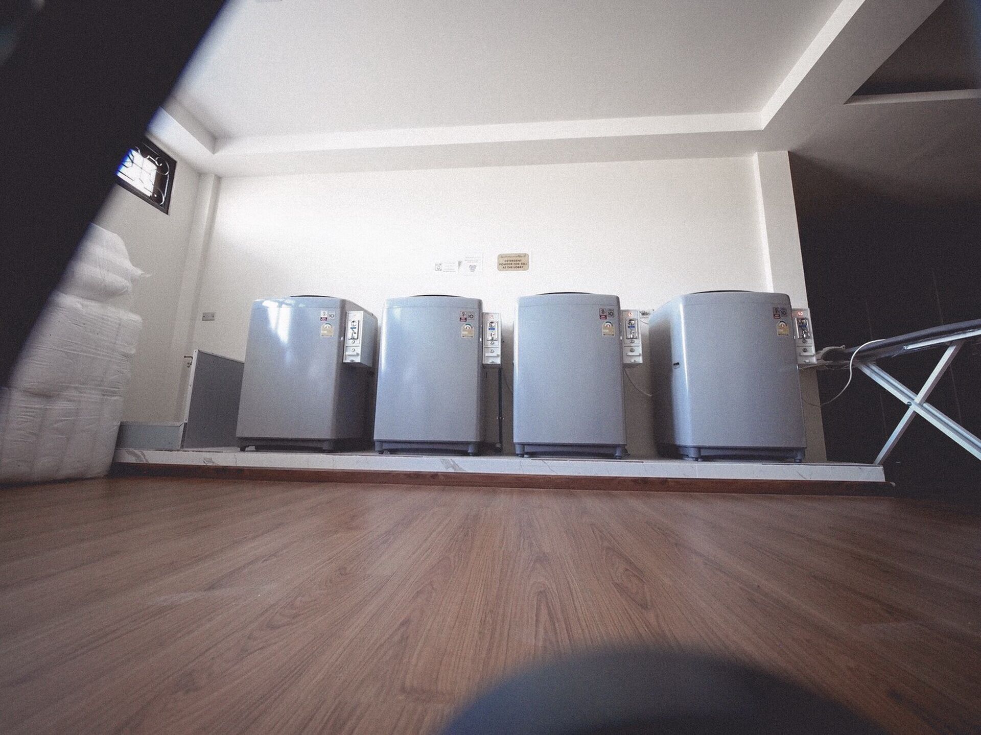 A room with four refrigerators lined up against a wall, a wooden floor, and a staircase leading to a landing.