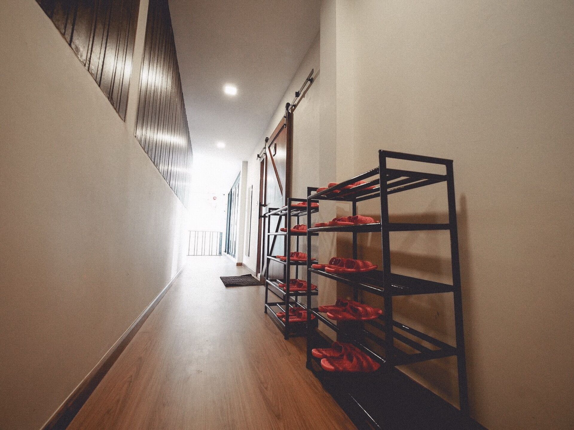 A hallway with wooden flooring and metal shoe racks on the right.