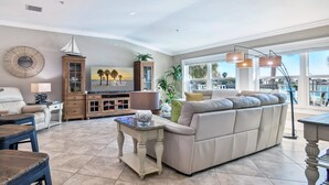 A spacious living room with a large beige sofa, a wooden cabinet, a television, and a view of the outdoors.
