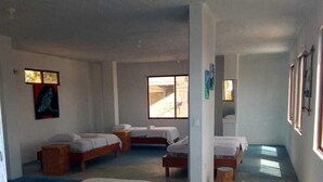 A dormitory room with bunk beds, a small wooden table, and a window providing natural light.