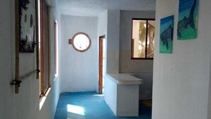 A narrow hallway with a blue floor, a wooden stool, and artwork on the walls.