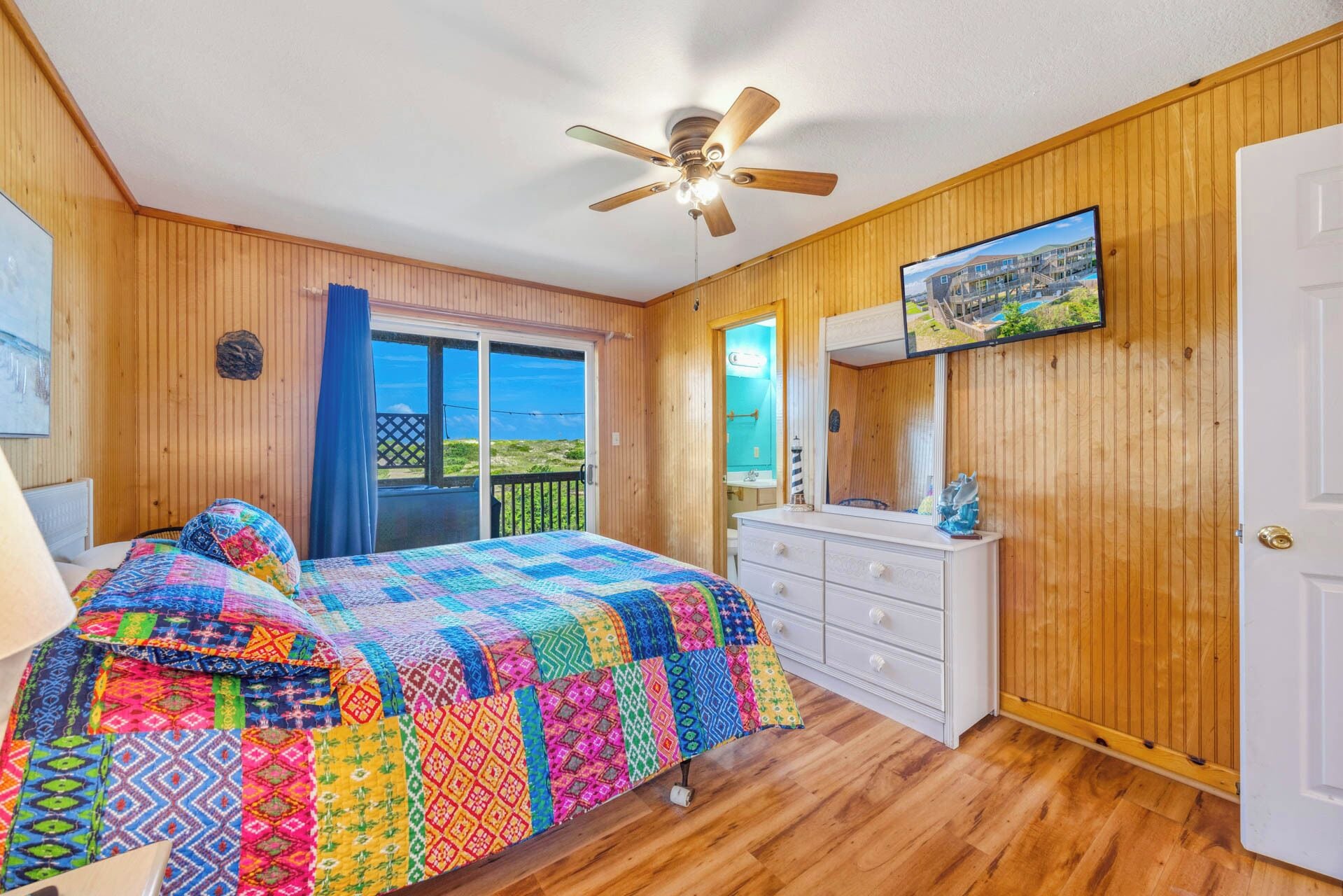 Ein Schlafzimmer mit Bett, Schminktisch, Deckenventilator, Fernseher und einem Balkon mit Blick.