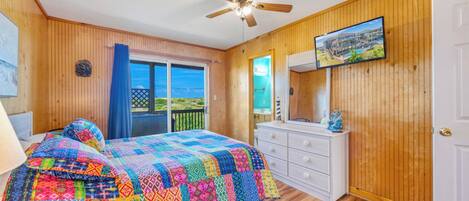 Ein Schlafzimmer mit Bett, Schminktisch, Deckenventilator, Fernseher und einem Balkon mit Blick.