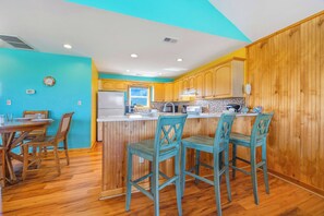 Una cocina con armarios de madera, una isla central con taburetes de bar y un comedor con mesa y sillas.