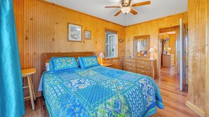 Une chambre à coucher aux murs lambrissés, comprenant un lit, une commode, une table de chevet et un ventilateur de plafond.