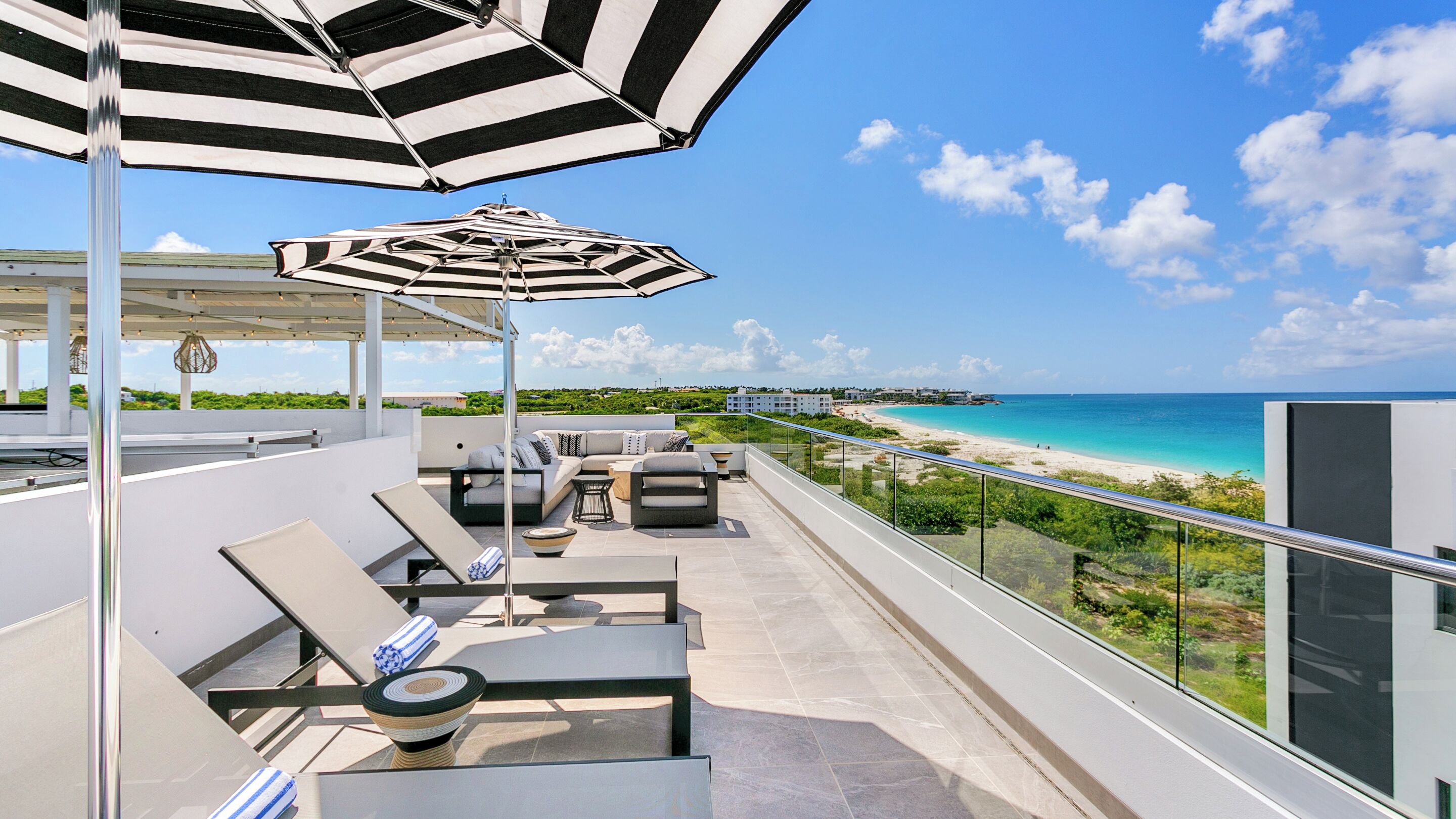 A rooftop terrace with a view of the beach, outdoor seating, and a large umbrella.
