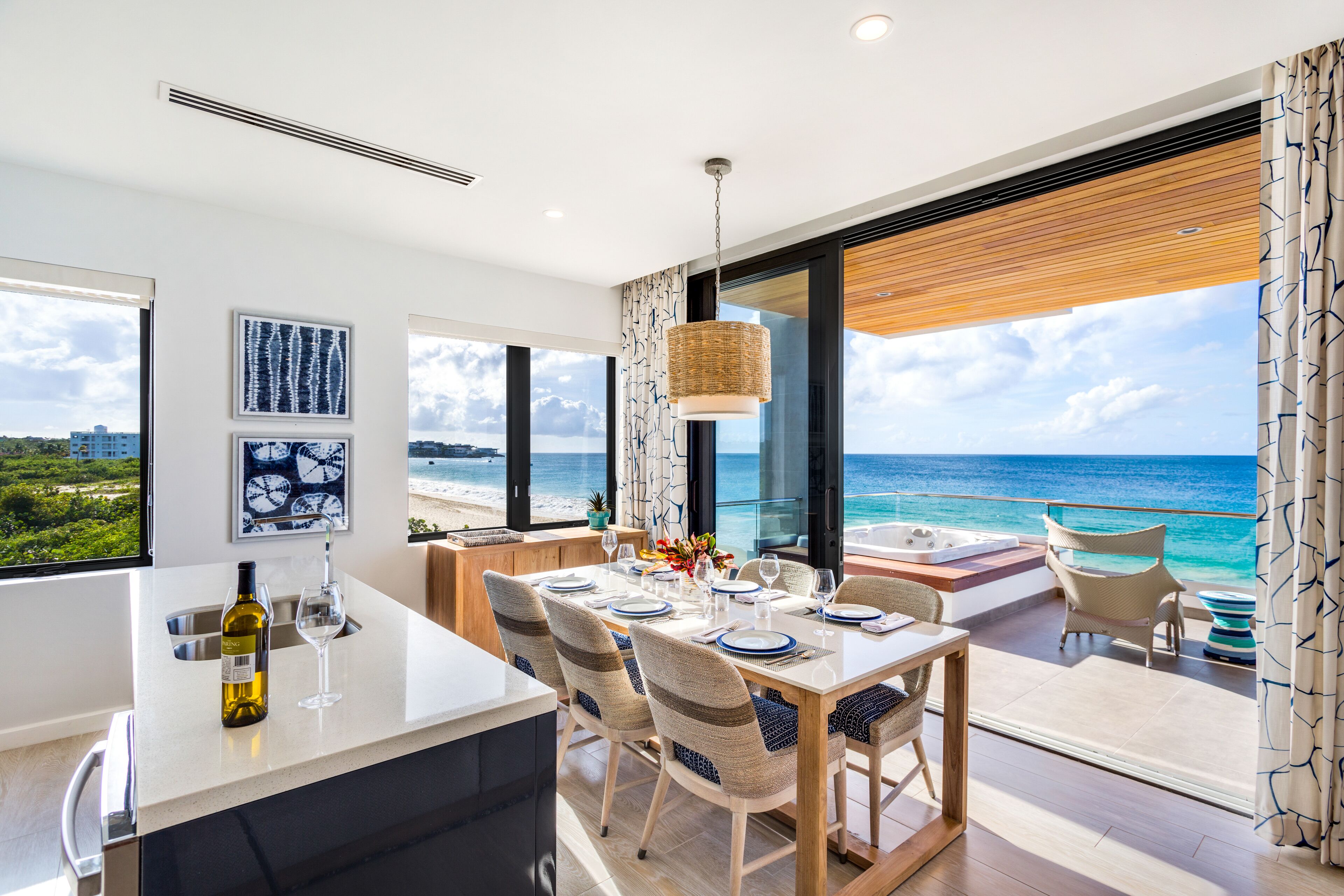 Un espace repas moderne avec vue sur l’océan, une grande fenêtre et une table à manger dressée avec des assiettes et des verres.