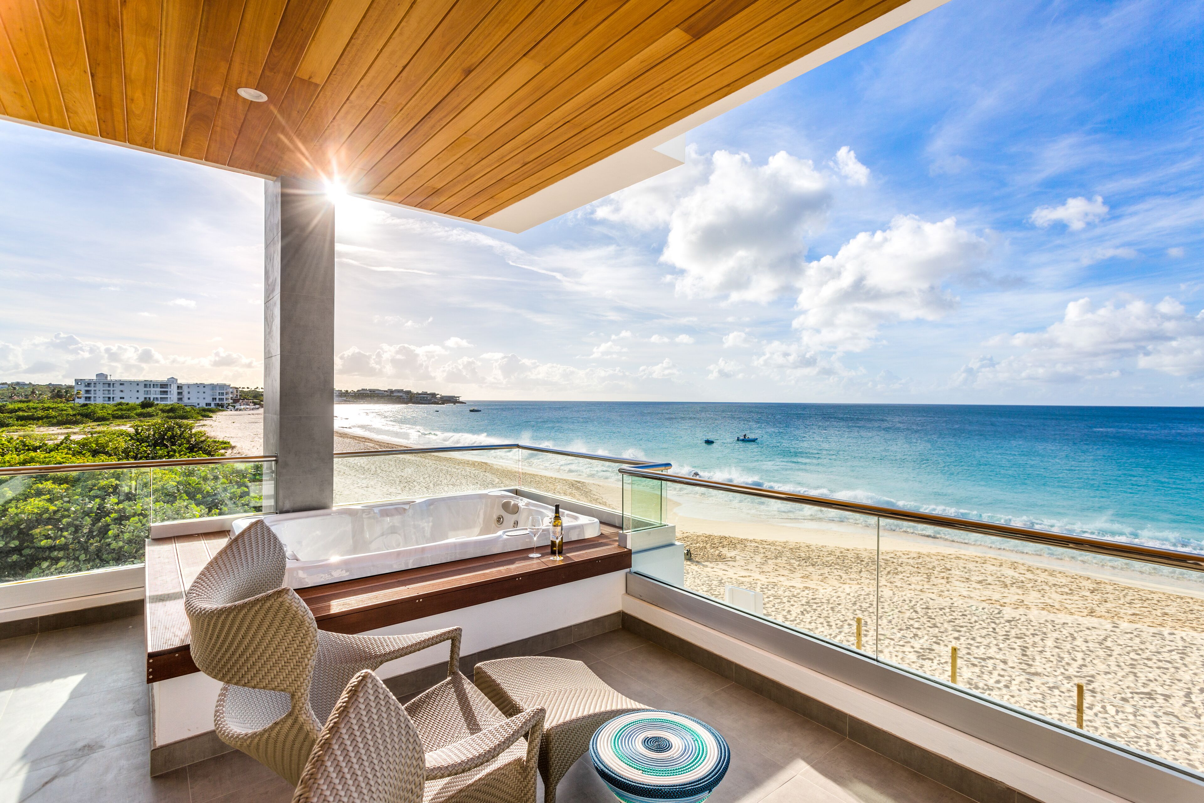 A balcony with a view of the beach and ocean, a hot tub, wicker chairs, and a round table.