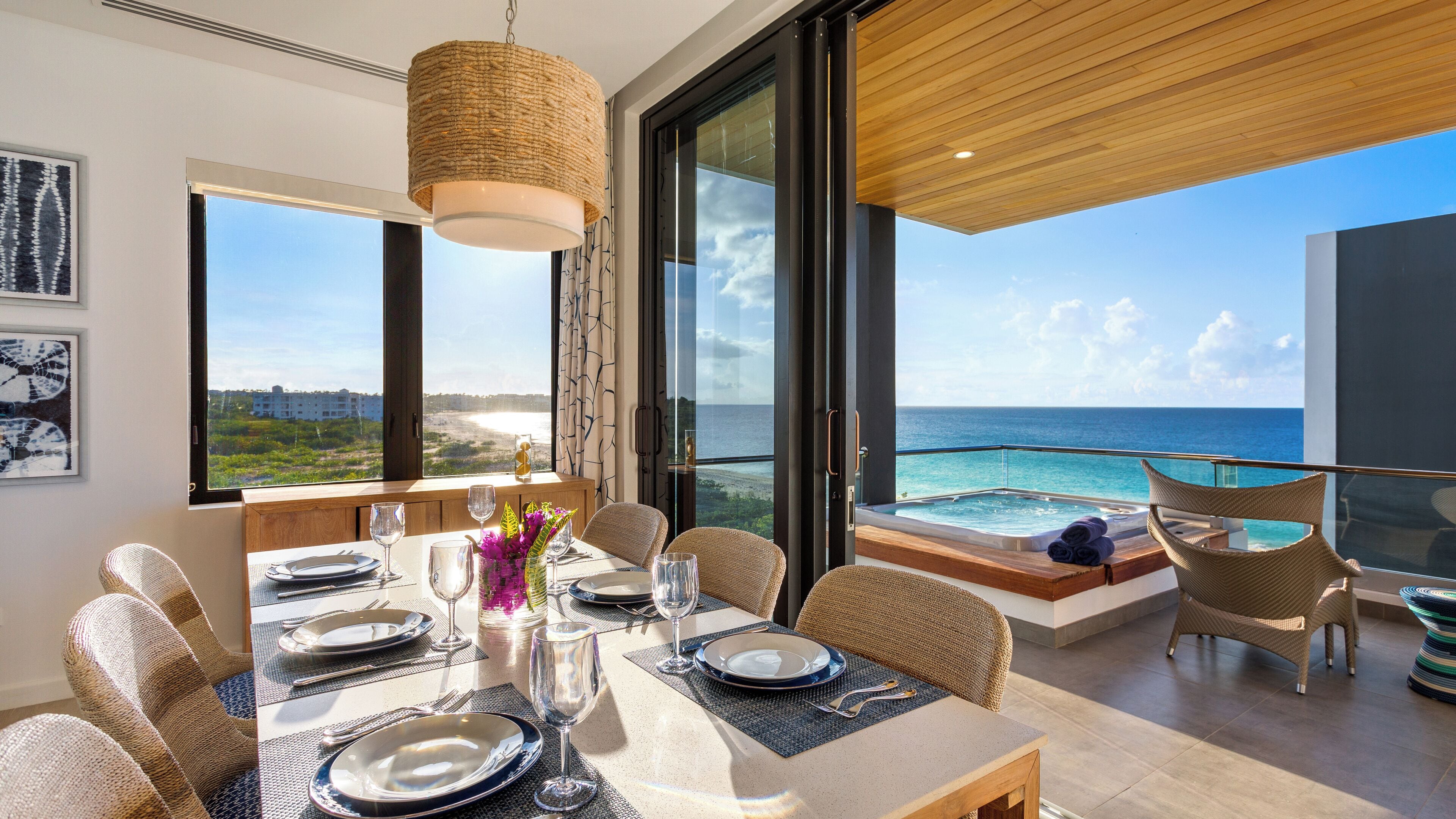 Comedor con mesa lista para cuatro, con vistas a una piscina y al océano.