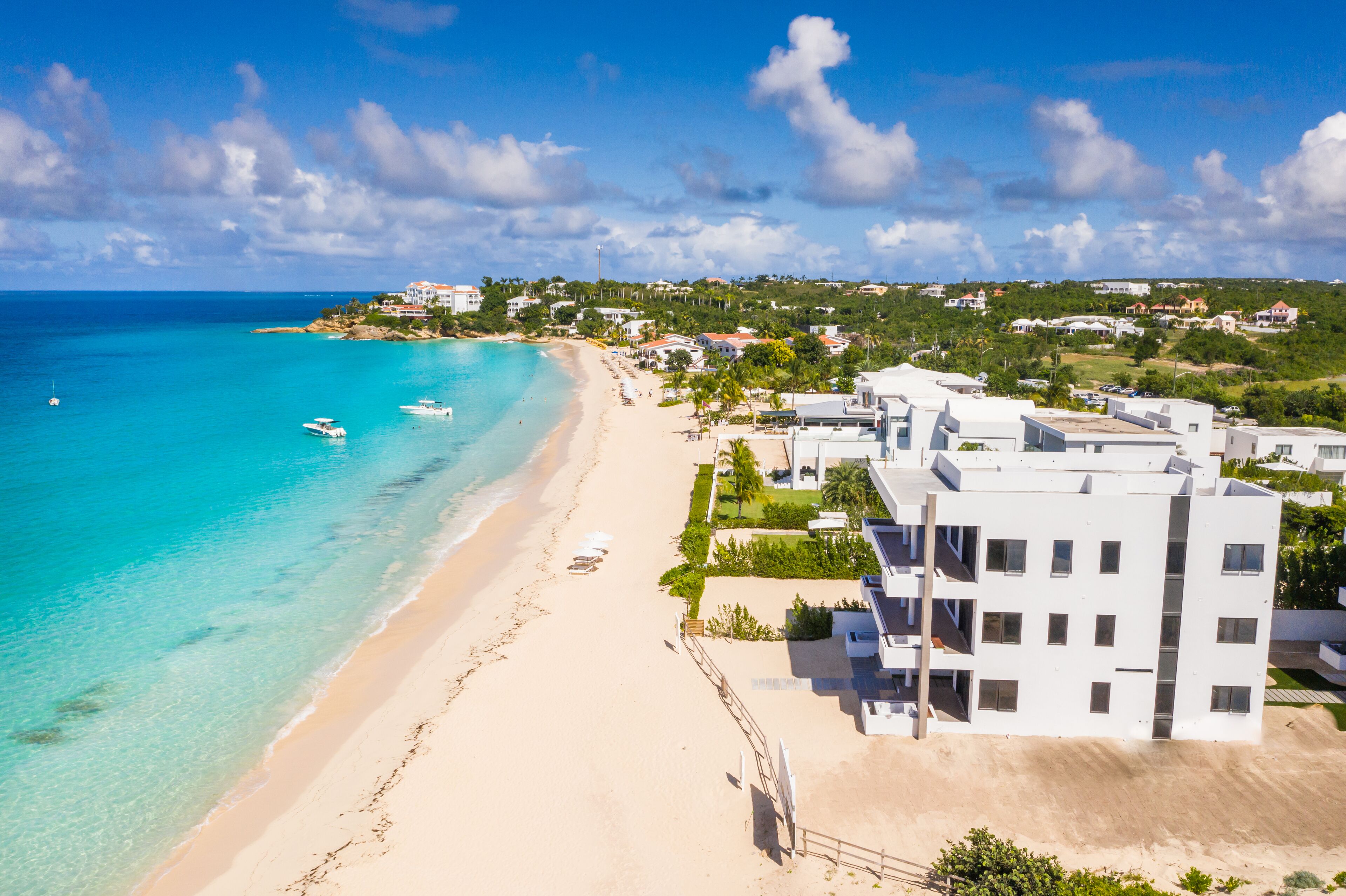 A coastal hotel with a beach view, modern architecture, and a clear sky.