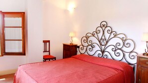 Ein Schlafzimmer mit einem großen Bett, einem Nachttisch aus Holz, einem Sessel und einem dekorativen Metall-Kopfende.