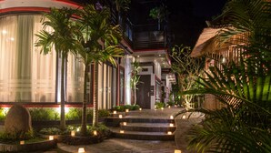 A well-lit hotel entrance with a curved facade, steps leading up to the entrance, and a thatched-roof structure nearby. - De Sarann Villa (Siem Reap)