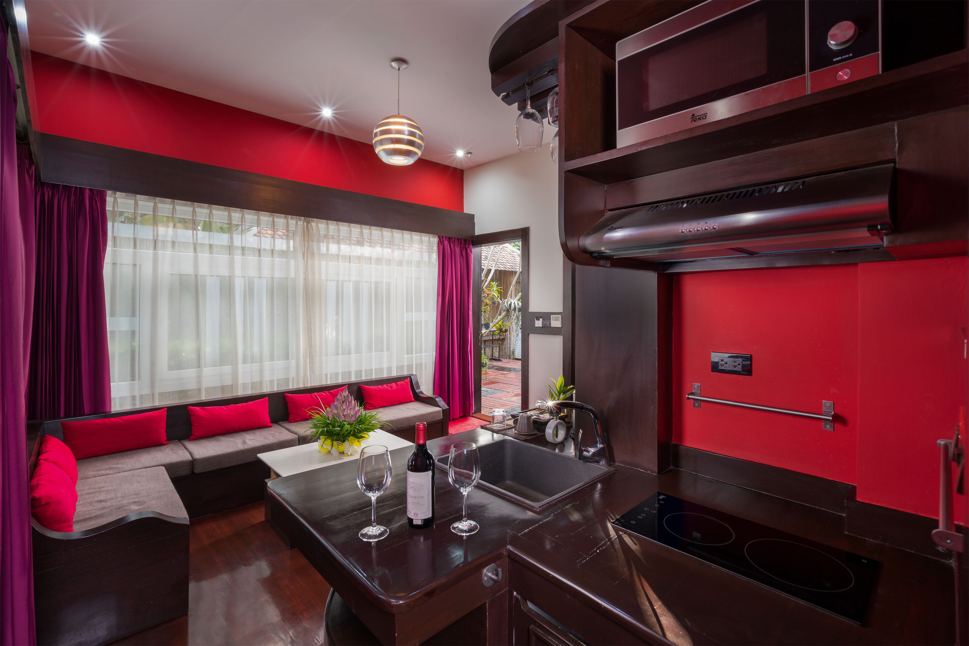 A modern kitchen with a red accent wall, a built-in oven, and a dining area with a sofa and table.