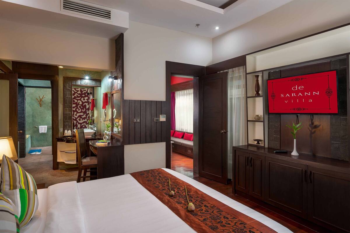 A hotel room with a bed, a desk, a chair, a vanity with a mirror, a TV on the wall, and a red sign.