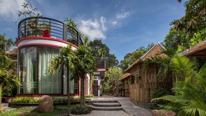 A modern building with a circular glass structure, surrounded by tropical vegetation and a wooden fence. - De Sarann Villa (Siem Reap)