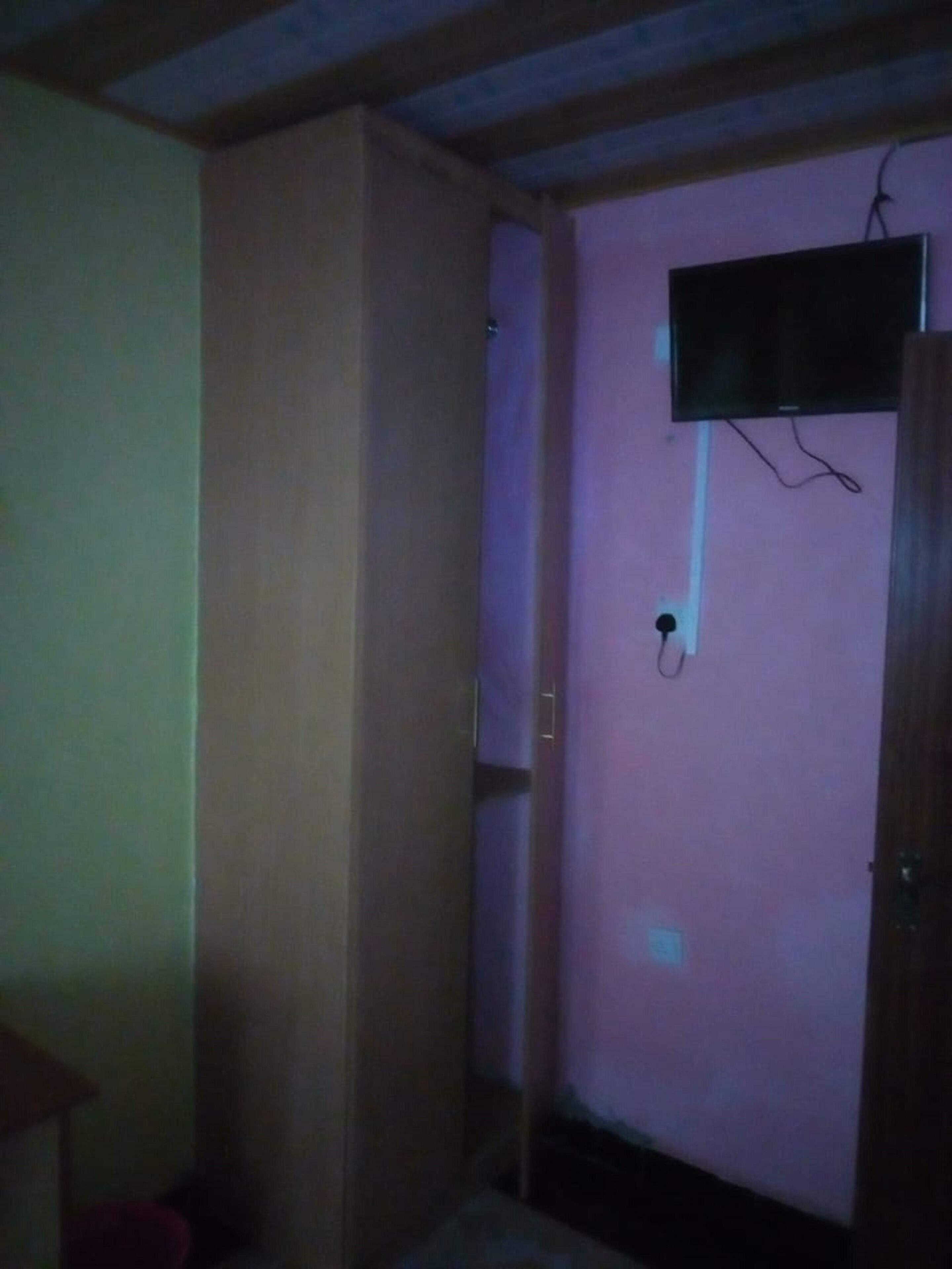 Una habitación con una televisión montada en la pared, una puerta y una pequeña mesa.