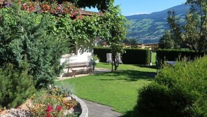 Un jardin avec un banc en bois, un mur blanc et une vue sur les montagnes.