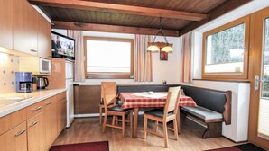Une cuisine compacte dotée de meubles en bois, d’un four à micro-ondes et d’une machine à café. On y trouve également un coin repas avec une table, des chaises et un banc.