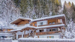 Un chalet en bois à plusieurs étages, doté d’un balcon et entouré d’arbres couverts de neige.