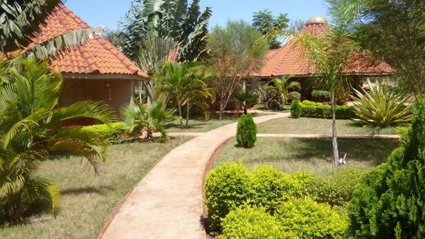 A pathway leading to a series of buildings with red-tiled roofs, surrounded by lush greenery and palm trees. - Philadelphia Retreat and Conference (Mururi)