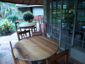 A wooden table and chairs in an outdoor patio area with a view of a garden and a building in the background.