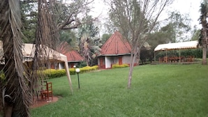 A grassy area with a few trees, a small building with a red roof, and a structure with a white roof. - Philadelphia Retreat and Conference (Mururi)