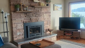 A living room with a stone fireplace, a flat-screen TV, and a sofa with cushions.