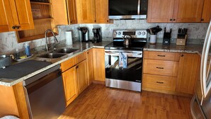 A kitchen with wooden cabinets, stainless steel appliances, a microwave, a coffee maker, and a kettle.