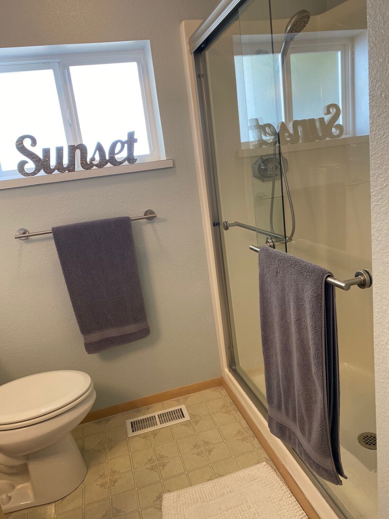 Et badeværelse med toilet, bruser med glasdør og et vindue med ordet "Sunset".