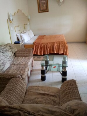 A bedroom with a bed, two patterned sofas, a glass coffee table, and a bedside table with a lamp. - Owoods Annex Hotel (Embu)
