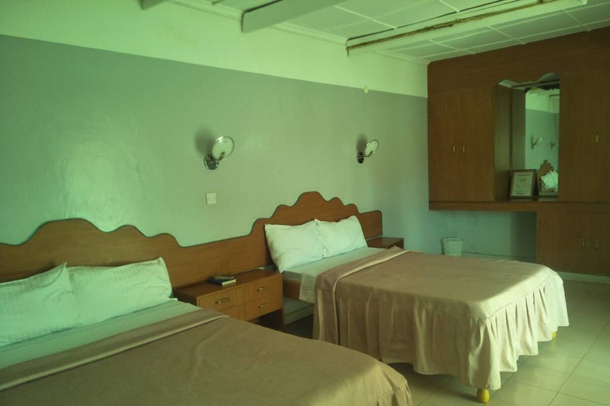 A hotel room with two single beds, a wooden wardrobe, a mirror, and a small bedside table.