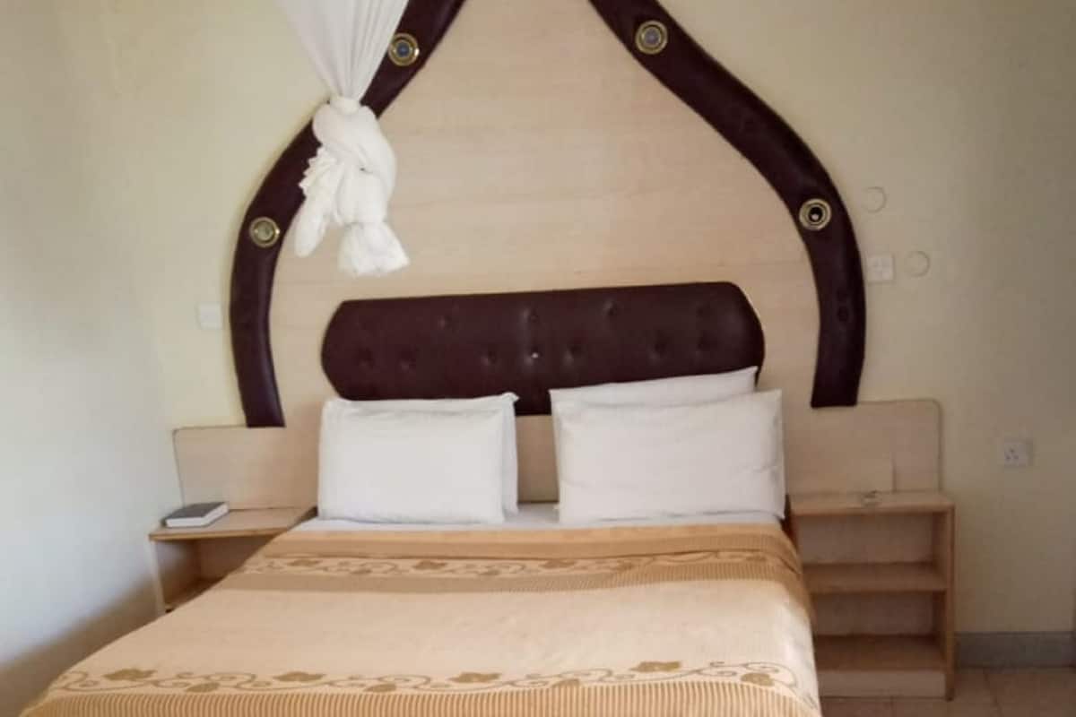 A bedroom with a bed, two bedside tables, a nightstand, a decorative headboard, and a patterned rug.