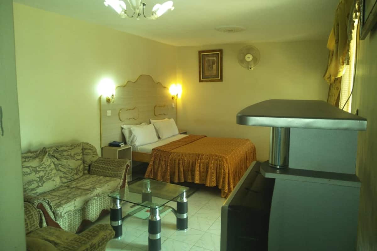 A bedroom with a bed, bedside lamps, a sofa, a glass-top coffee table, and a TV stand.