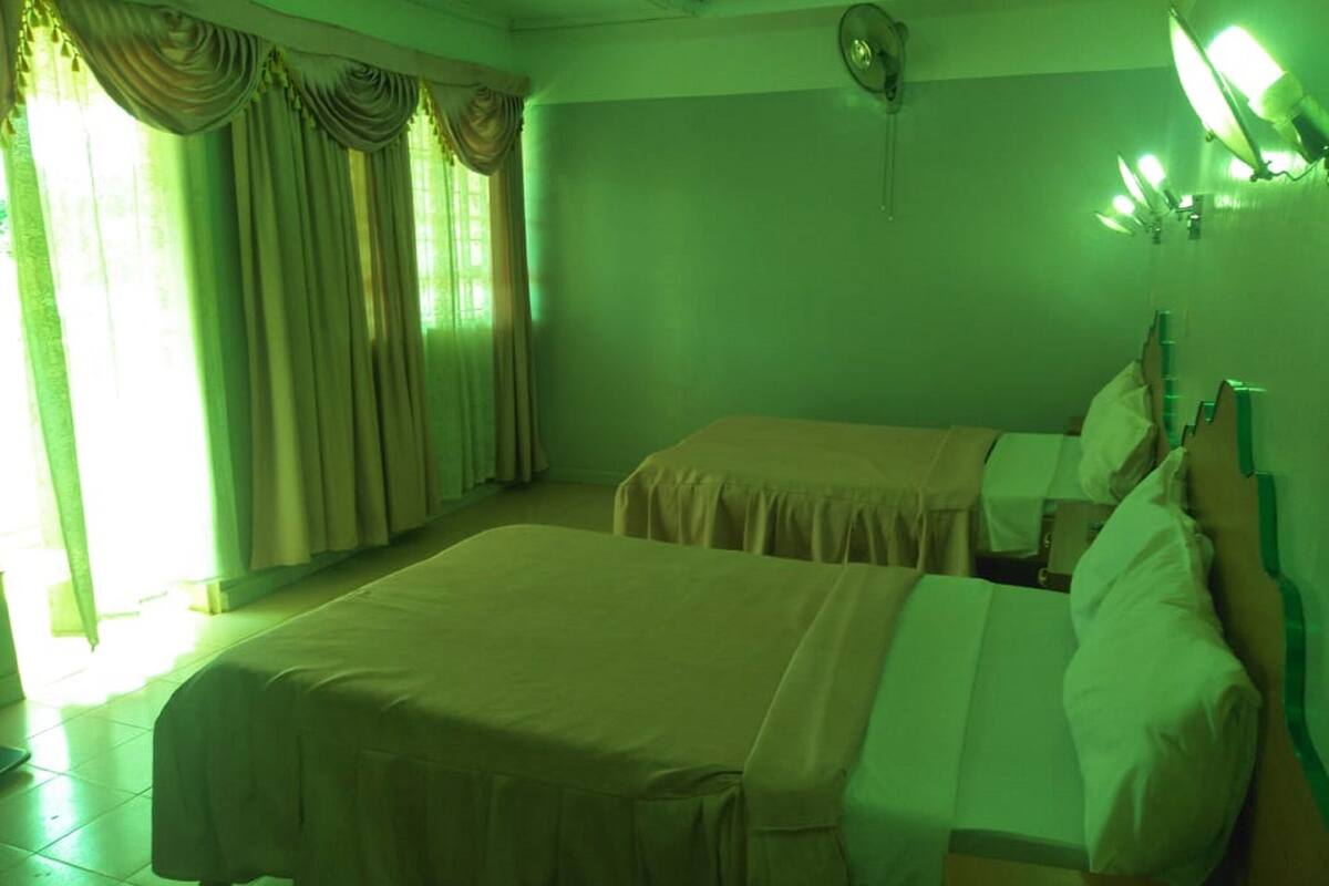 A room with two beds, a window with curtains, and a wall-mounted light fixture.
