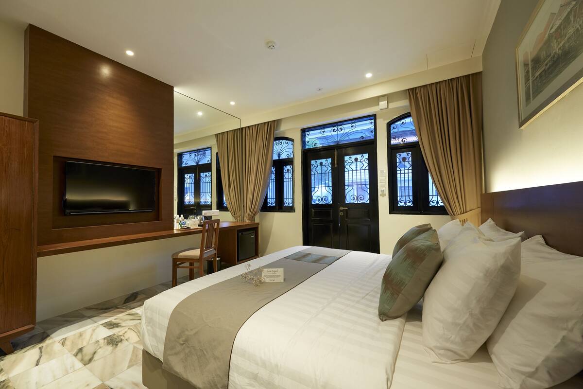 Habitación de hotel con una cama grande, un escritorio, una silla y un televisor montado en la pared.