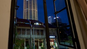 A view through a window of a tall building with a lit sign, a traditional building, and a street view at night. - Macalister Terraces Hotel (George Town)