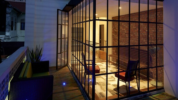 A modern glass-enclosed room with a wooden deck, a bench, and a view of a tall building in the background. - Macalister Terraces Hotel (George Town)
