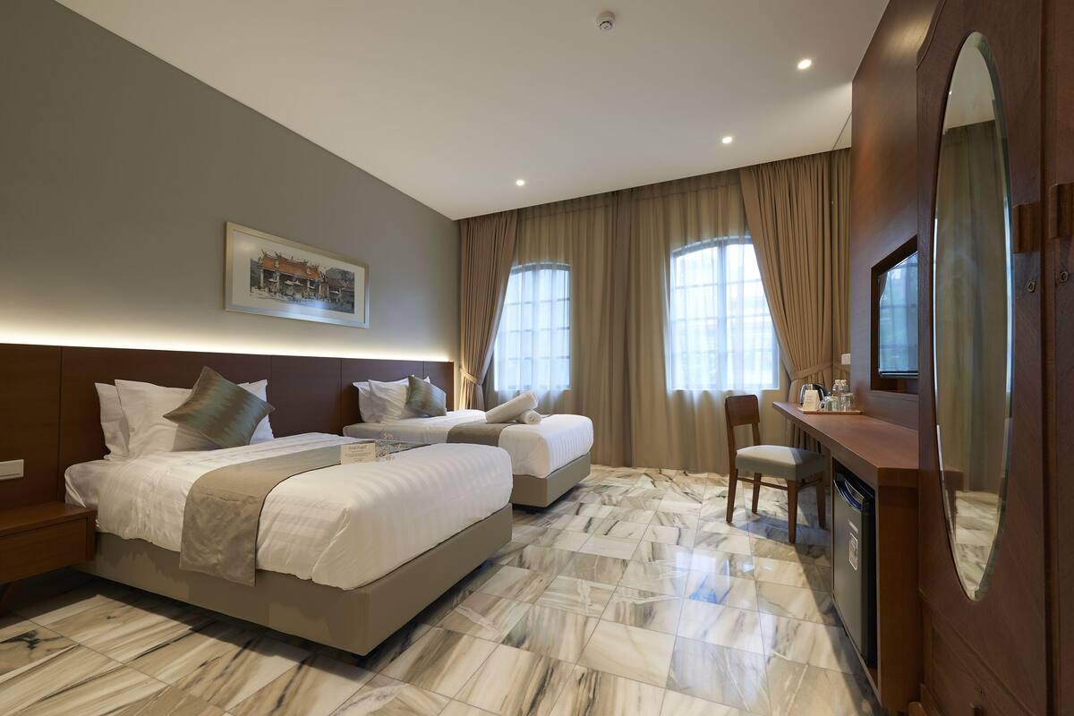 Una habitación de hotel con una cama grande, una cama más pequeña, un escritorio y una silla.