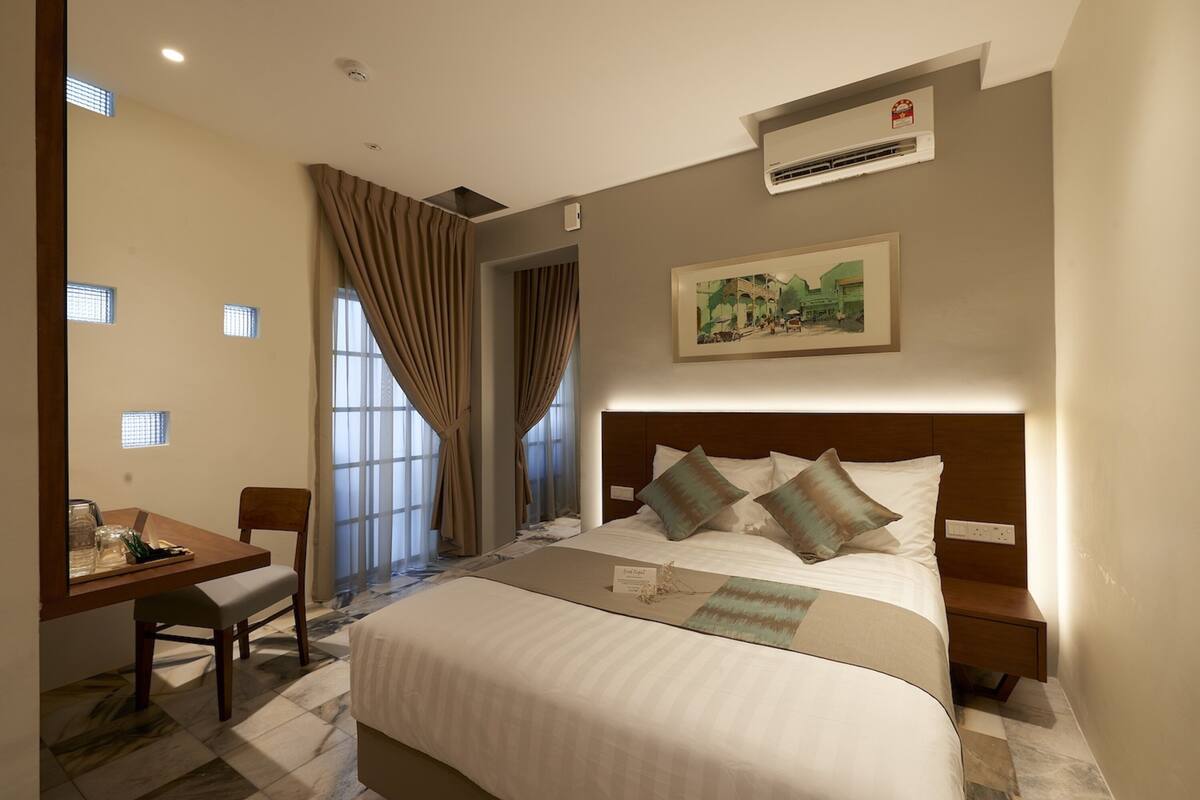 Habitación de hotel con cama, escritorio, silla y ventana con cortinas.