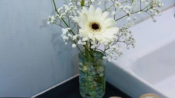 Un tocador de baño con un secador de pelo, un florero de vidrio con flores y dos botellas de vidrio vacías sobre una bandeja.