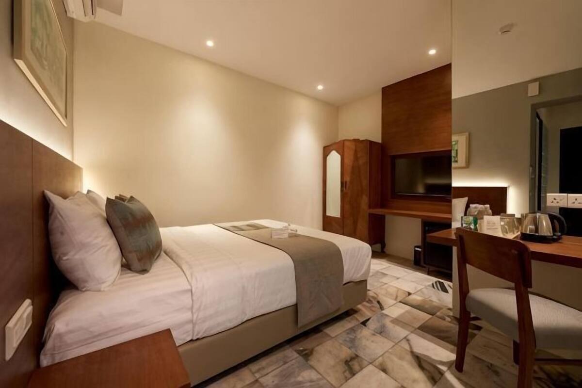 Habitación de hotel con cama, escritorio, silla, televisor y espejo.