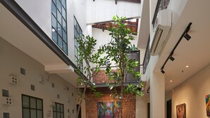 A spacious indoor area with a high ceiling, a brick wall with a colorful painting, a sofa, chairs, a coffee table, and a patterned floor. - Macalister Terraces Hotel (George Town)