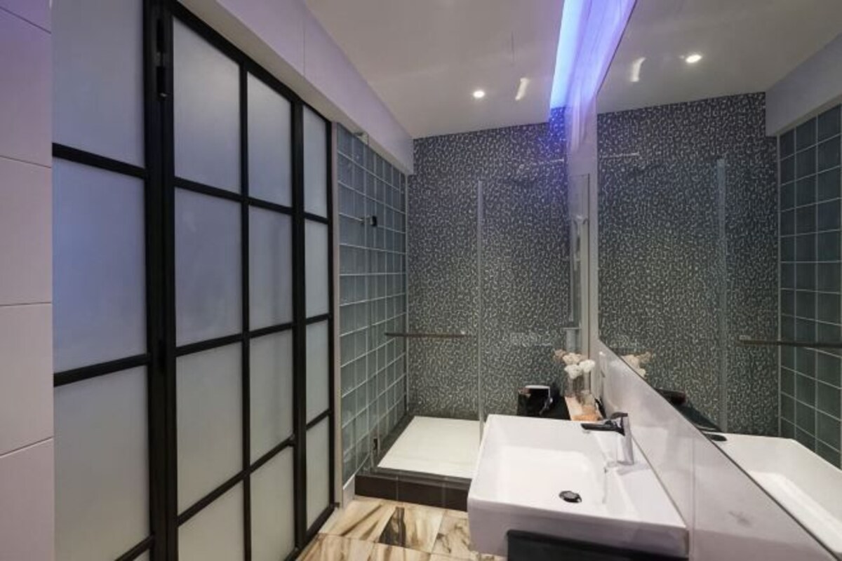 A modern bathroom with a glass shower enclosure, a white sink, and a marble floor.