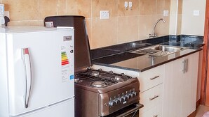 Een kleine keuken met een koelkast, fornuis, magnetron en kastjes.